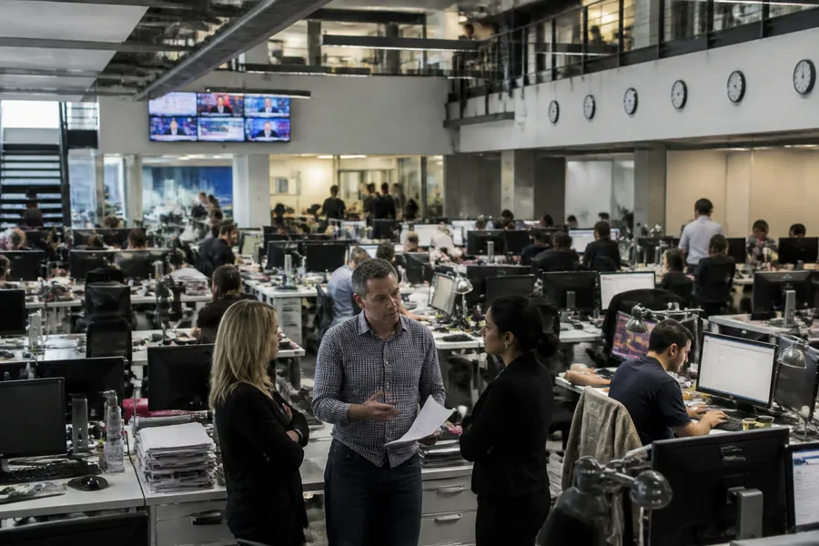 A busy newsroom desk with screens, notes and coffee, the daily reality behind the headlines